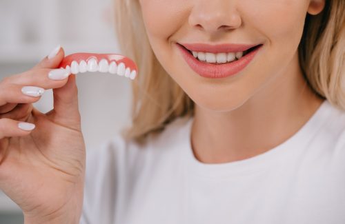 cropped view of smiling woman holding teeth cover